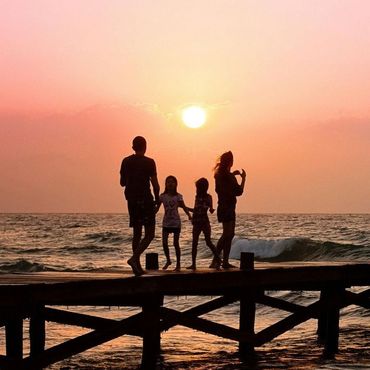 Eine Familie steht auf einem Pier und beobachtet den Sonnenuntergang über dem Meer