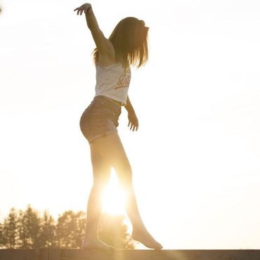 Eine Frau in einem bauchfreien Top und Shorts balanciert auf Mauer