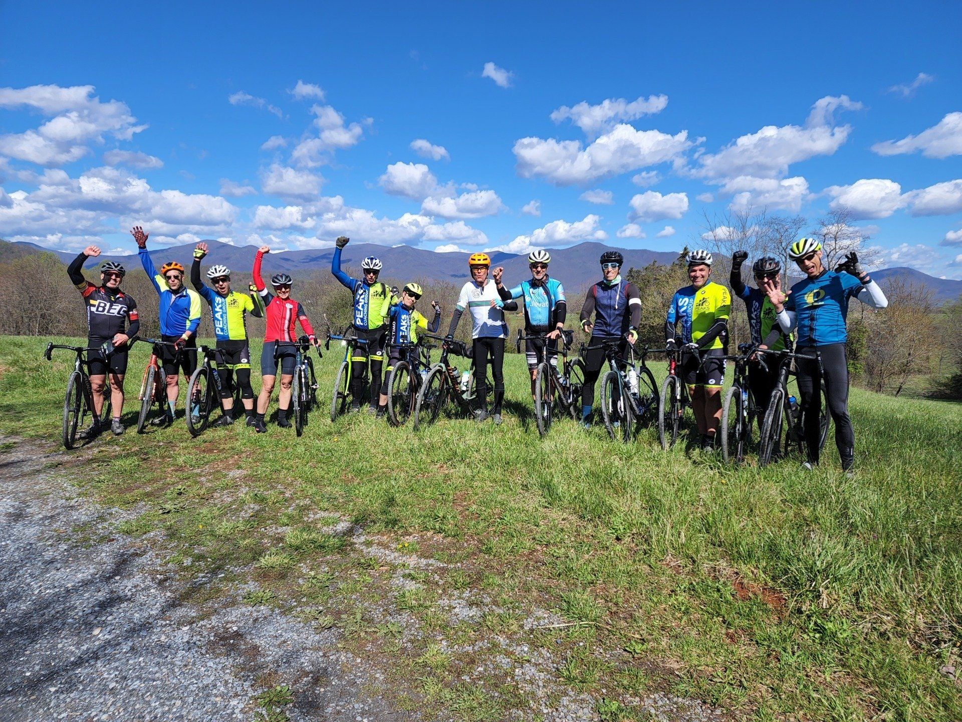 A group of cyclists are posing for a picture on top of a grassy hill.