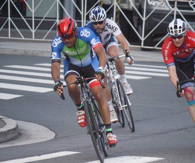 A group of cyclists are riding down a street and one of them is wearing a helmet that says aks