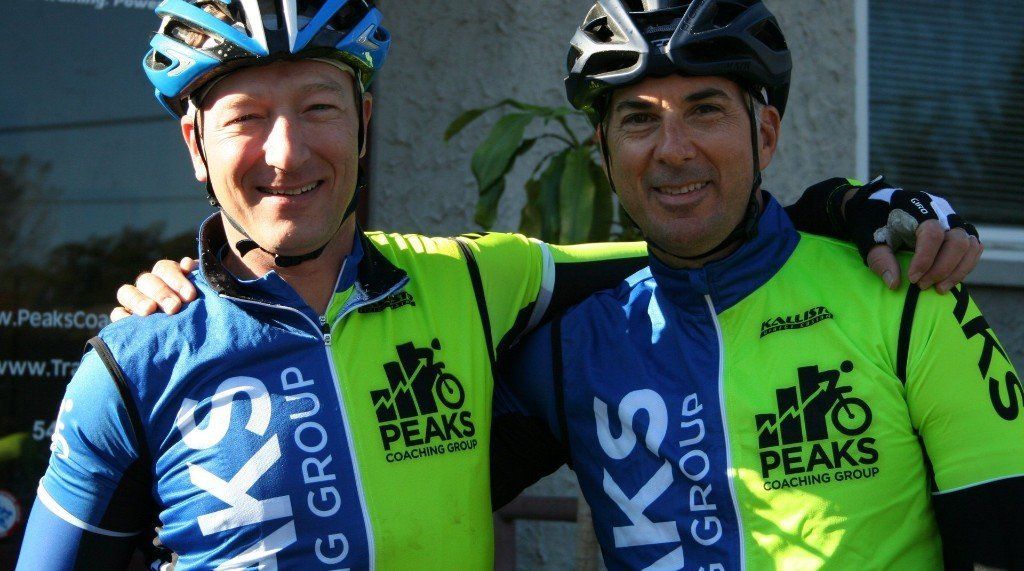Two men wearing peaks cycling jerseys are posing for a picture