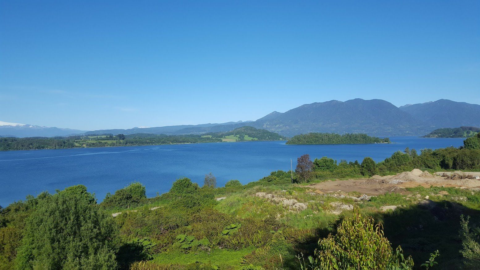 A large body of water surrounded by trees and mountains on a sunny day.