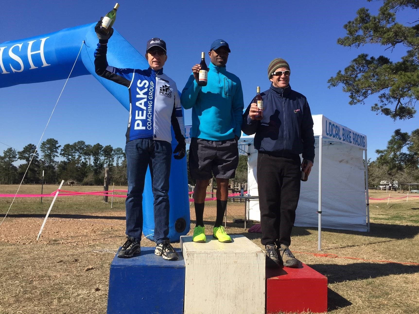 Three men standing on a podium with one wearing a shirt that says peaks
