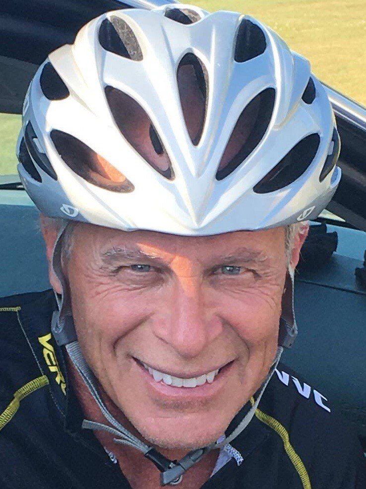 A man wearing a bicycle helmet is smiling for the camera