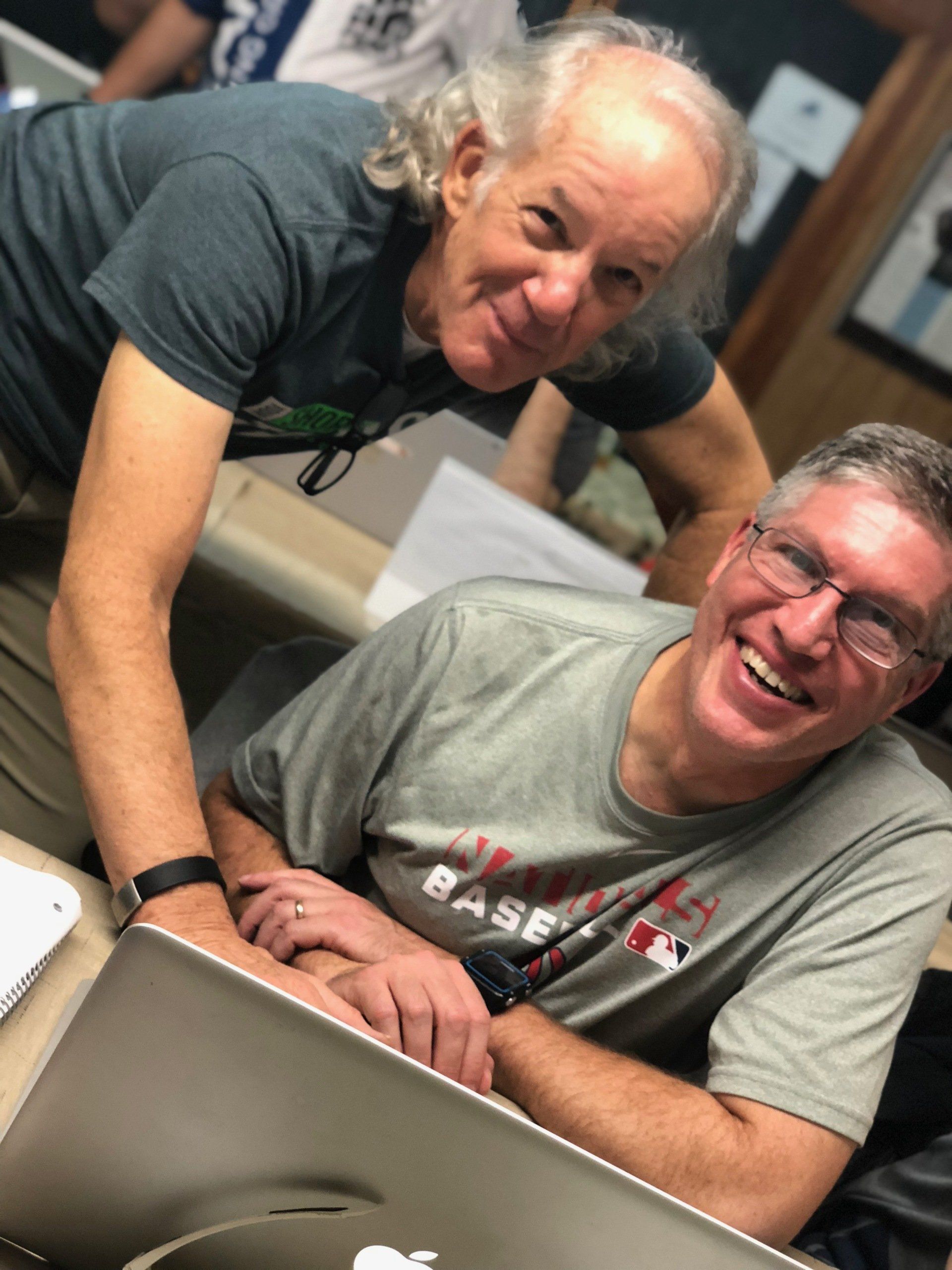 Two men are posing for a picture with one wearing a base ball shirt