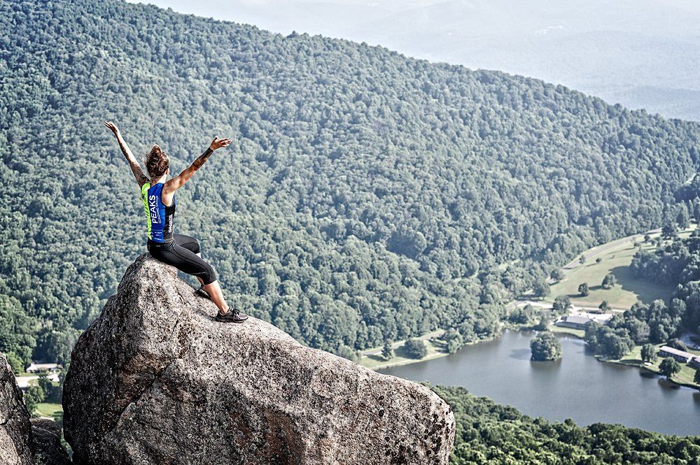 A woman is sitting on top of a large rock with her arms in the air.