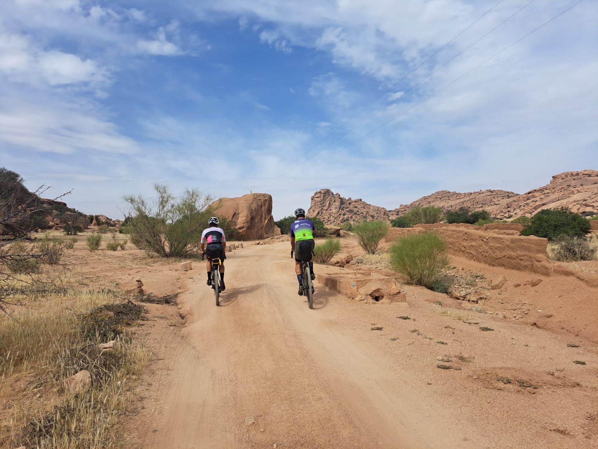Two people are riding bikes down a dirt road.