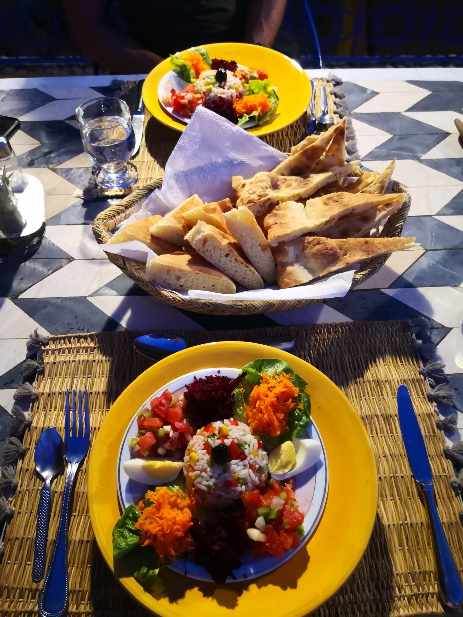 Two plates of food and a basket of bread are on a table.