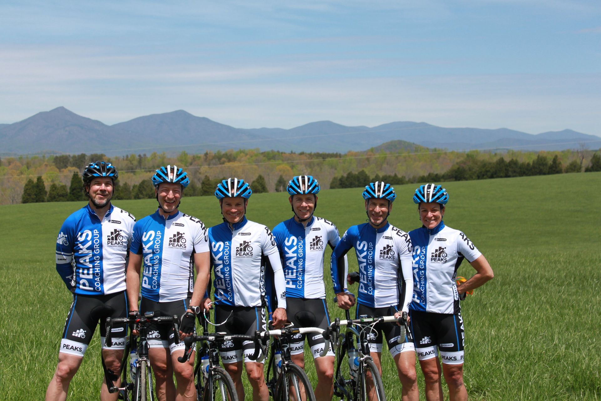 A group of cyclists standing in a field with mountains in the background