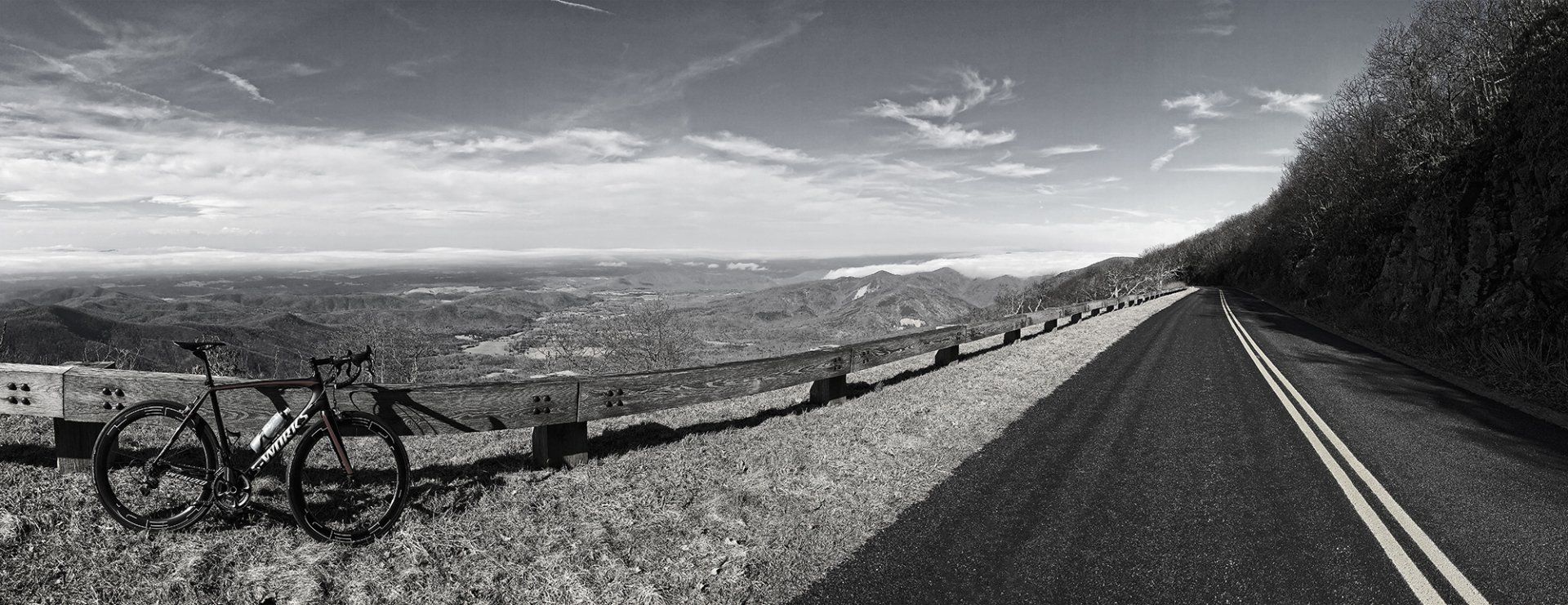 A black and white photo of a bicycle parked on the side of a road.