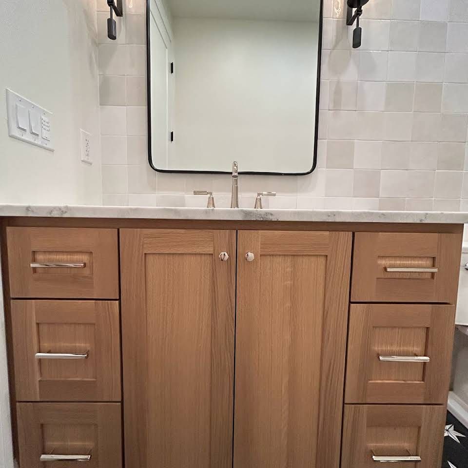 A bathroom vanity with wooden cabinets , drawers , a sink and a mirror.