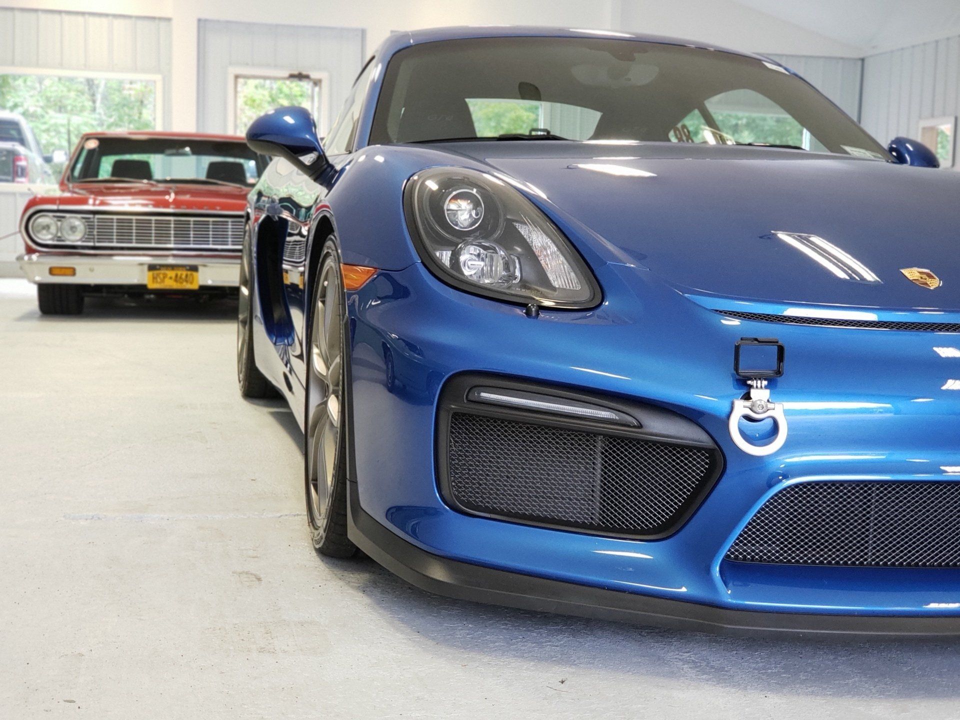 A blue car is parked in a garage next to a red car