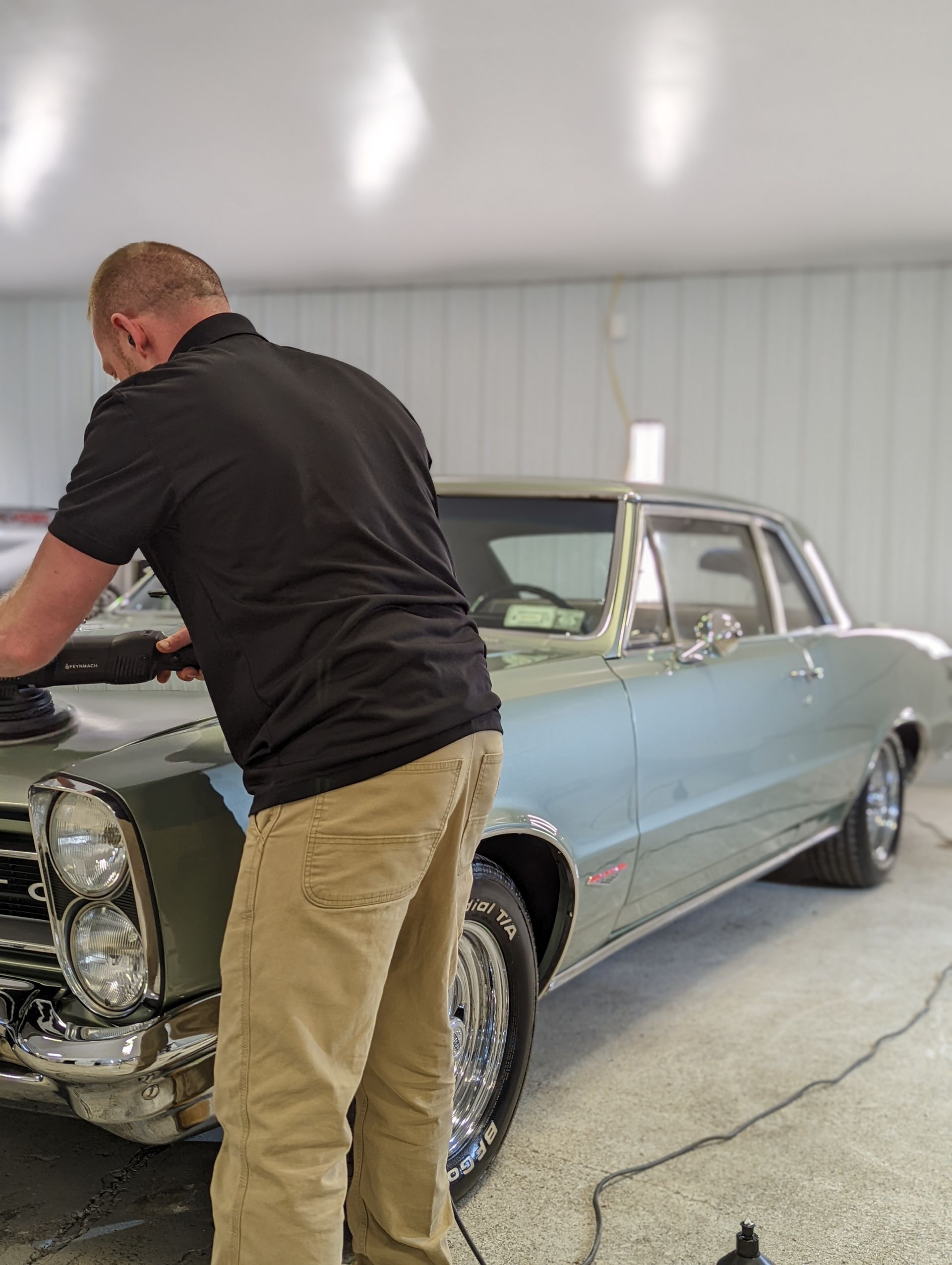 Blue Dodge Charger, rear quarter view, black wheels, inside garage, bright lighting.