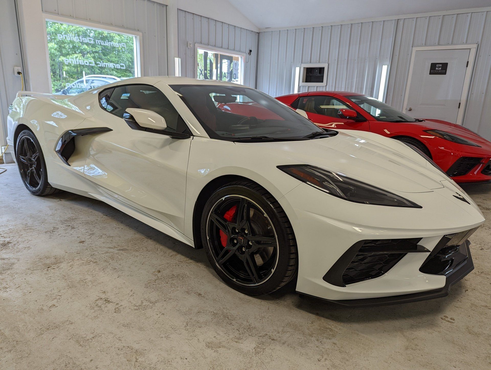 A white corvette is parked next to a red corvette in a garage.