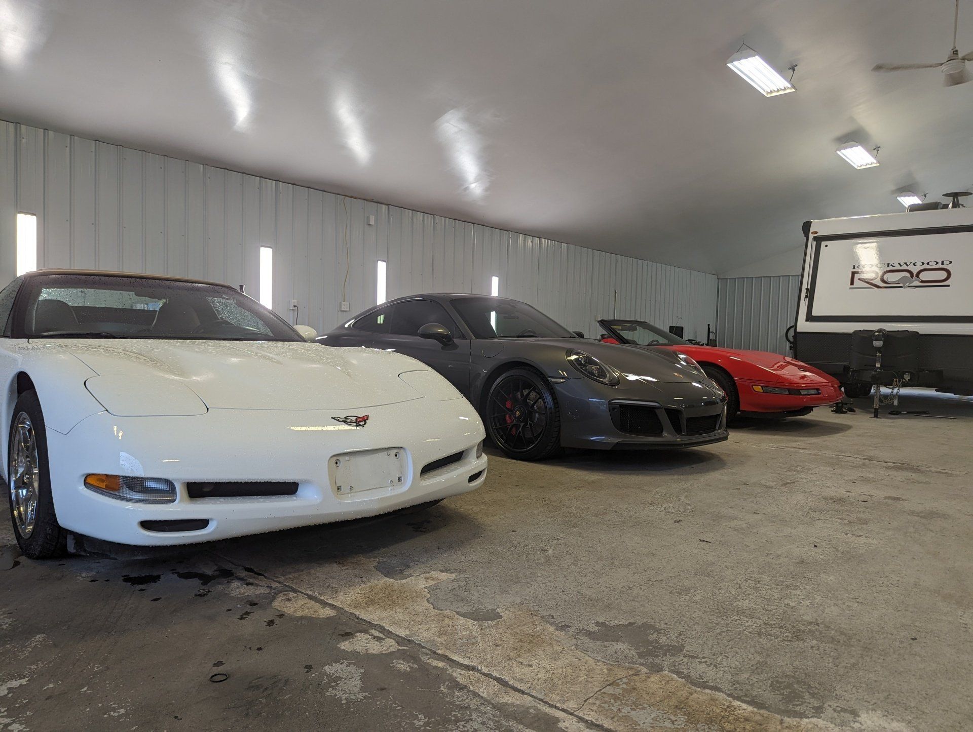 Three sports cars are parked in a garage next to a trailer.