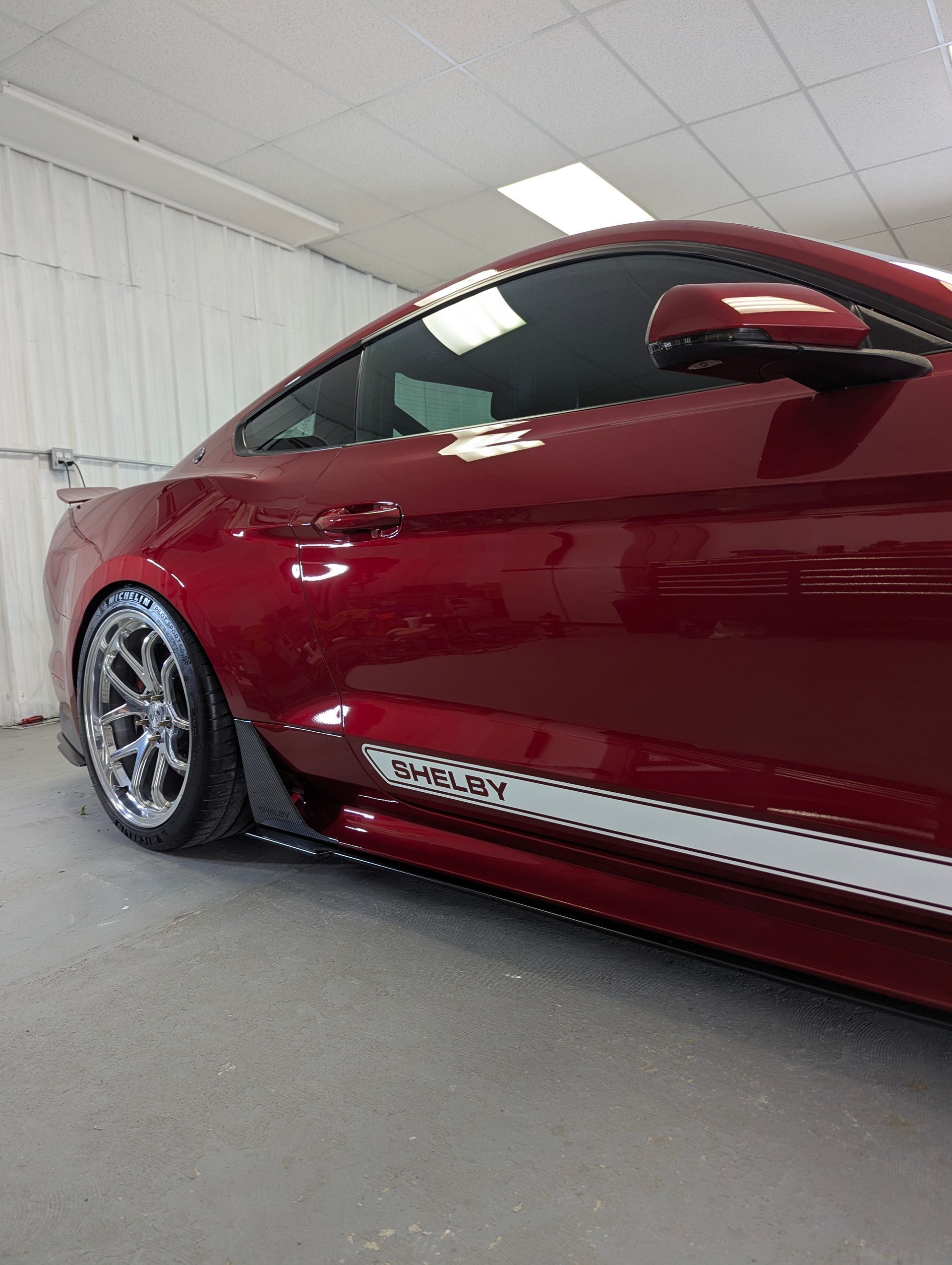 Red Ford Mustang with white stripes, custom wheels, in an indoor setting.