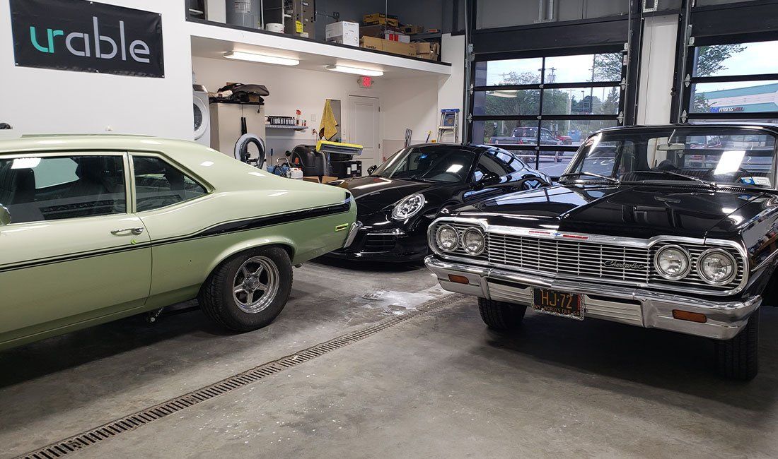 Two old cars are parked in a garage next to each other.