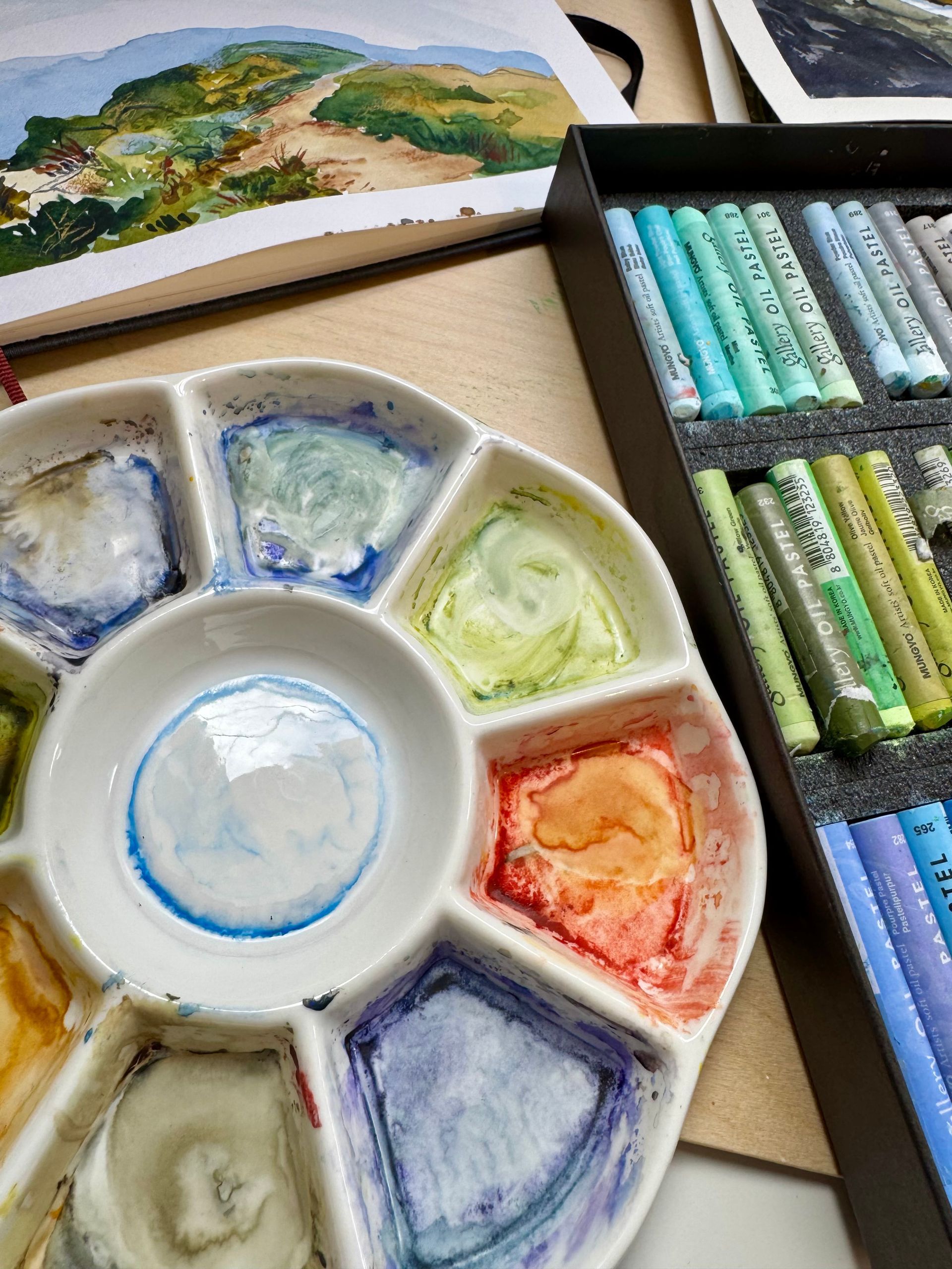 Met een kwast wordt op een houten palet bruine verf gemengd met klodders kleurrijke verf.