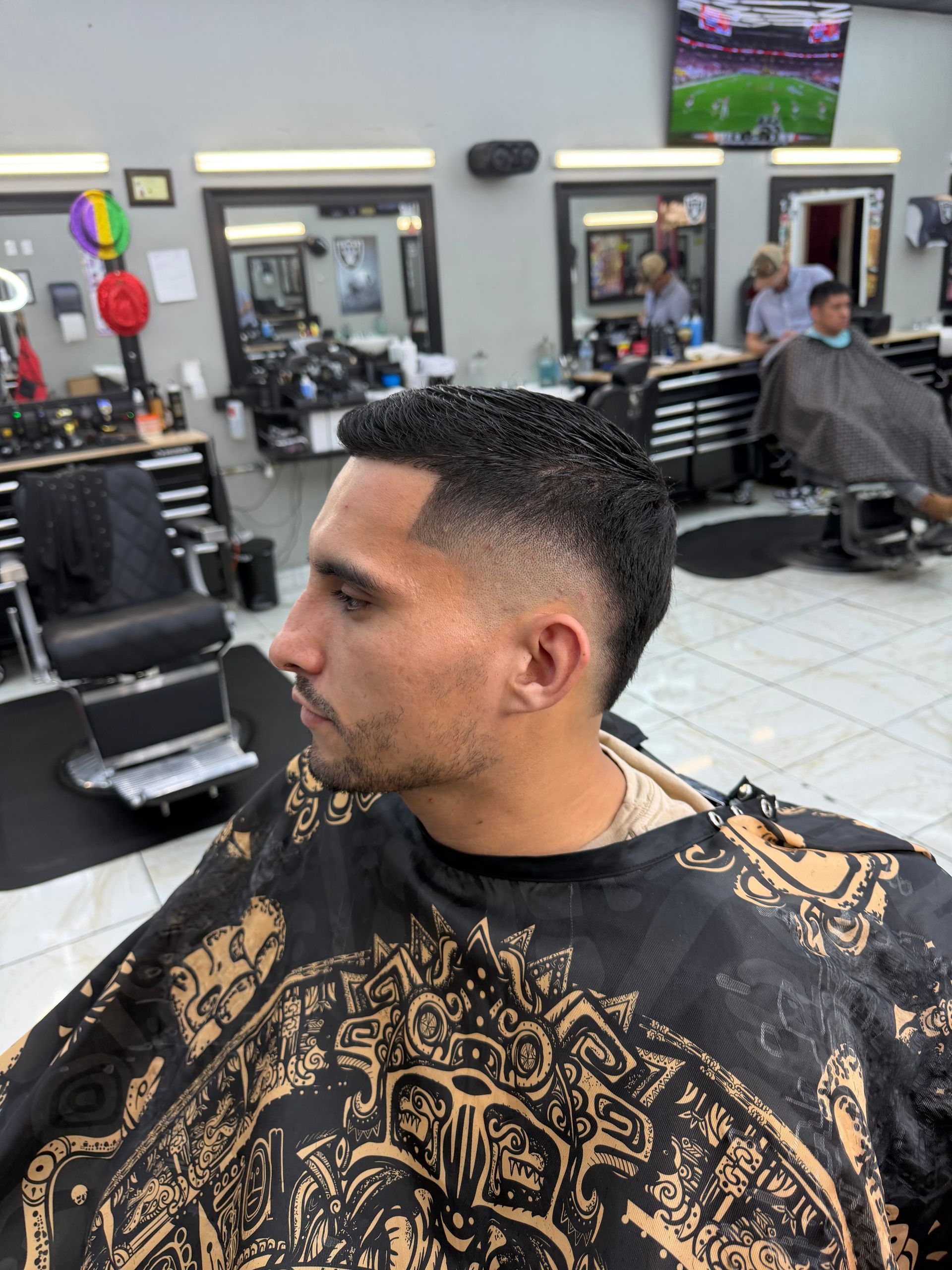 Man getting a haircut in a barbershop. He has a fade with textured hair. He's wearing a patterned cape.