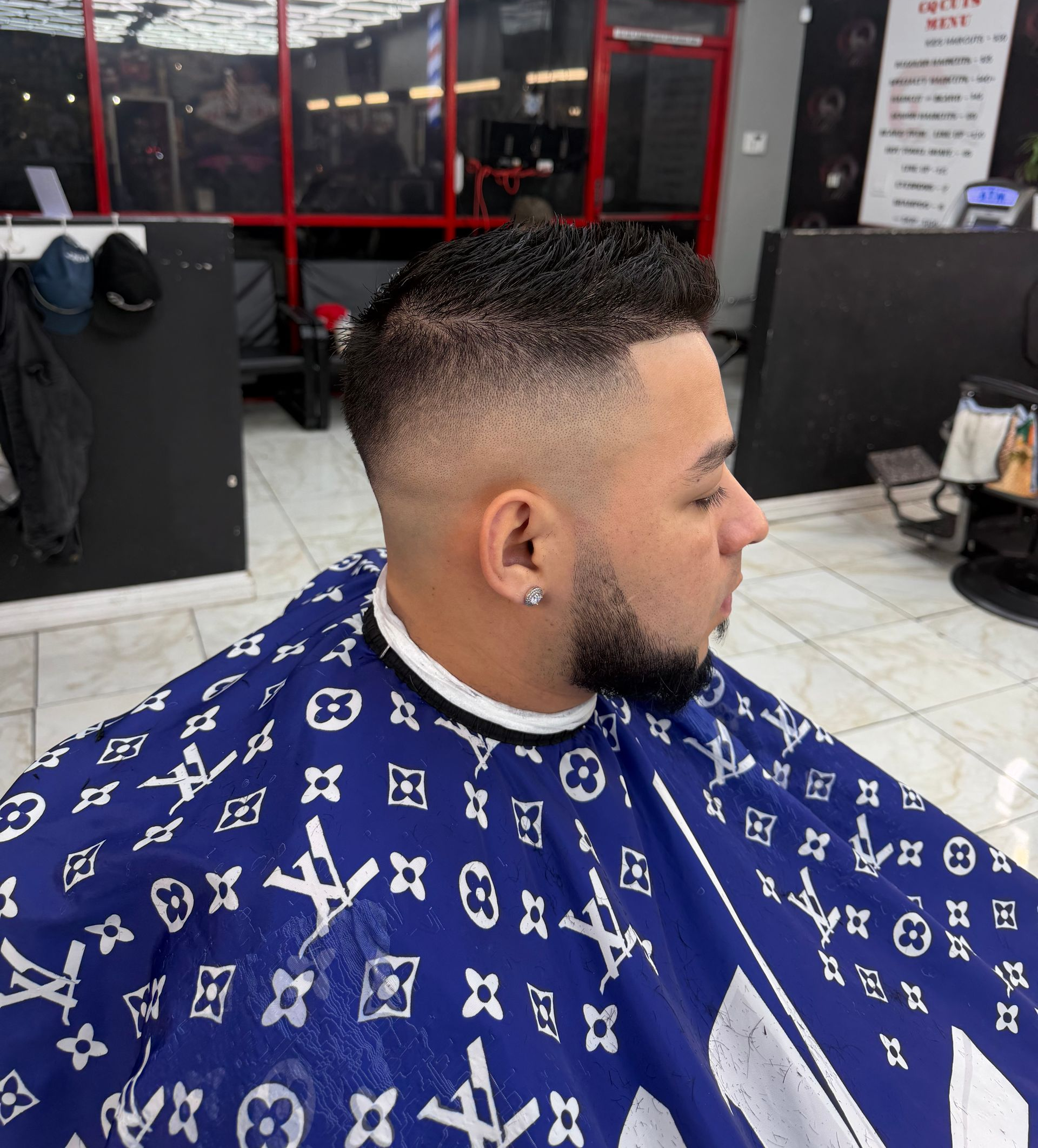 Man with a faded haircut at a barbershop, wearing a blue Louis Vuitton cape.