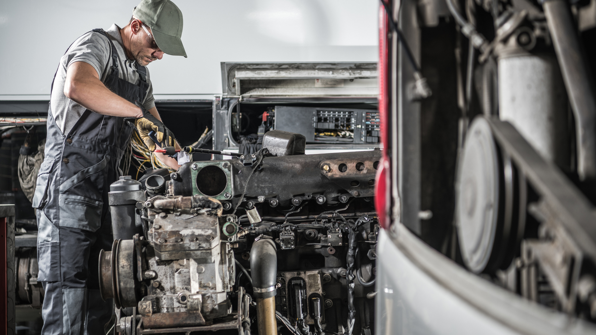 Mechanic working on an engine in a garage, with tools and a vehicle interior nearby.