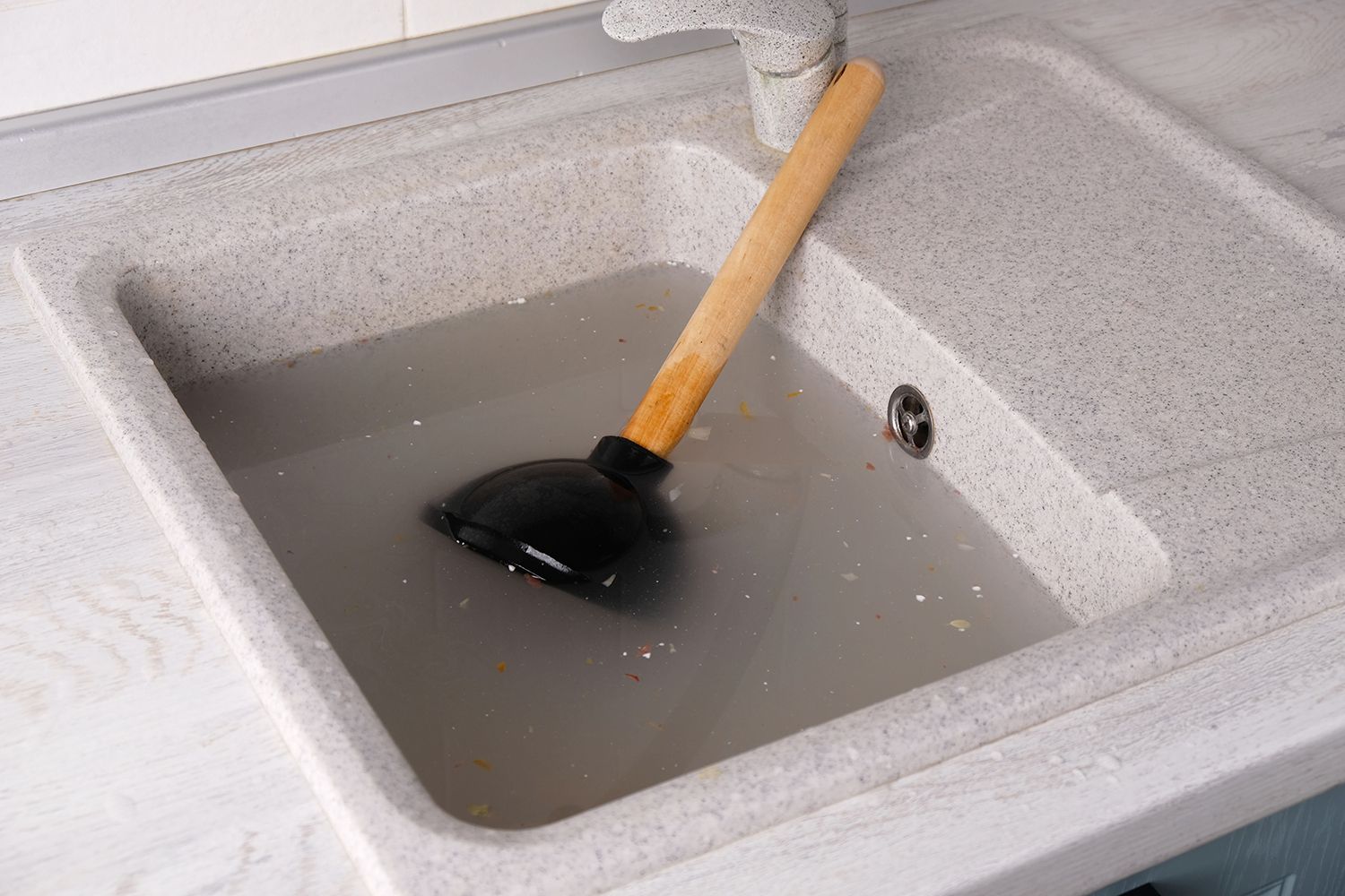 Kitchen sink filled with cloudy water and a plunger resting inside, showing a drainage issue. Kitchen sink filled with cloudy water and a plunger resting inside, showing a drainage issue.