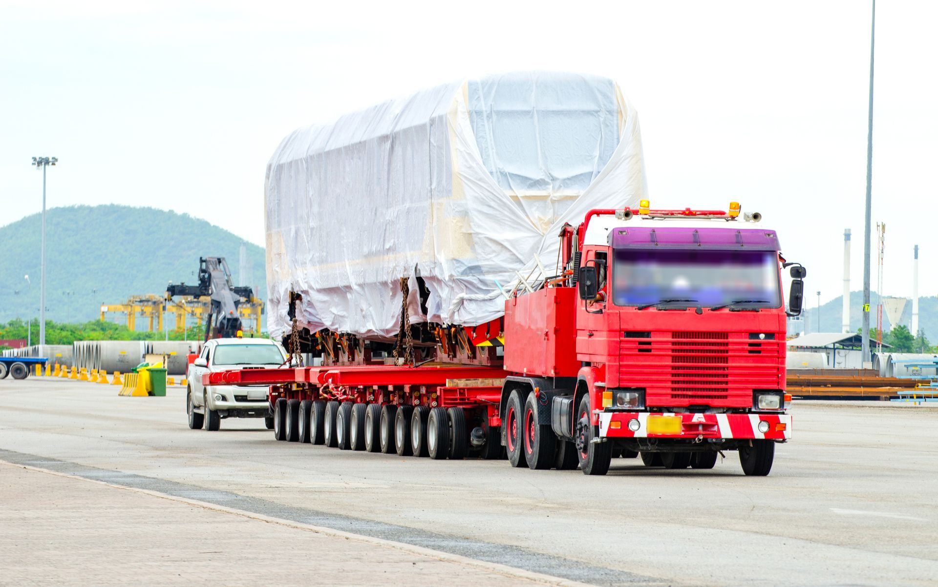 Red semi hauls wrapped cargo on multi-axle trailer down highway.