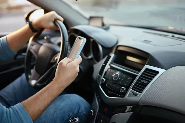 A man is driving a car and using a cell phone.