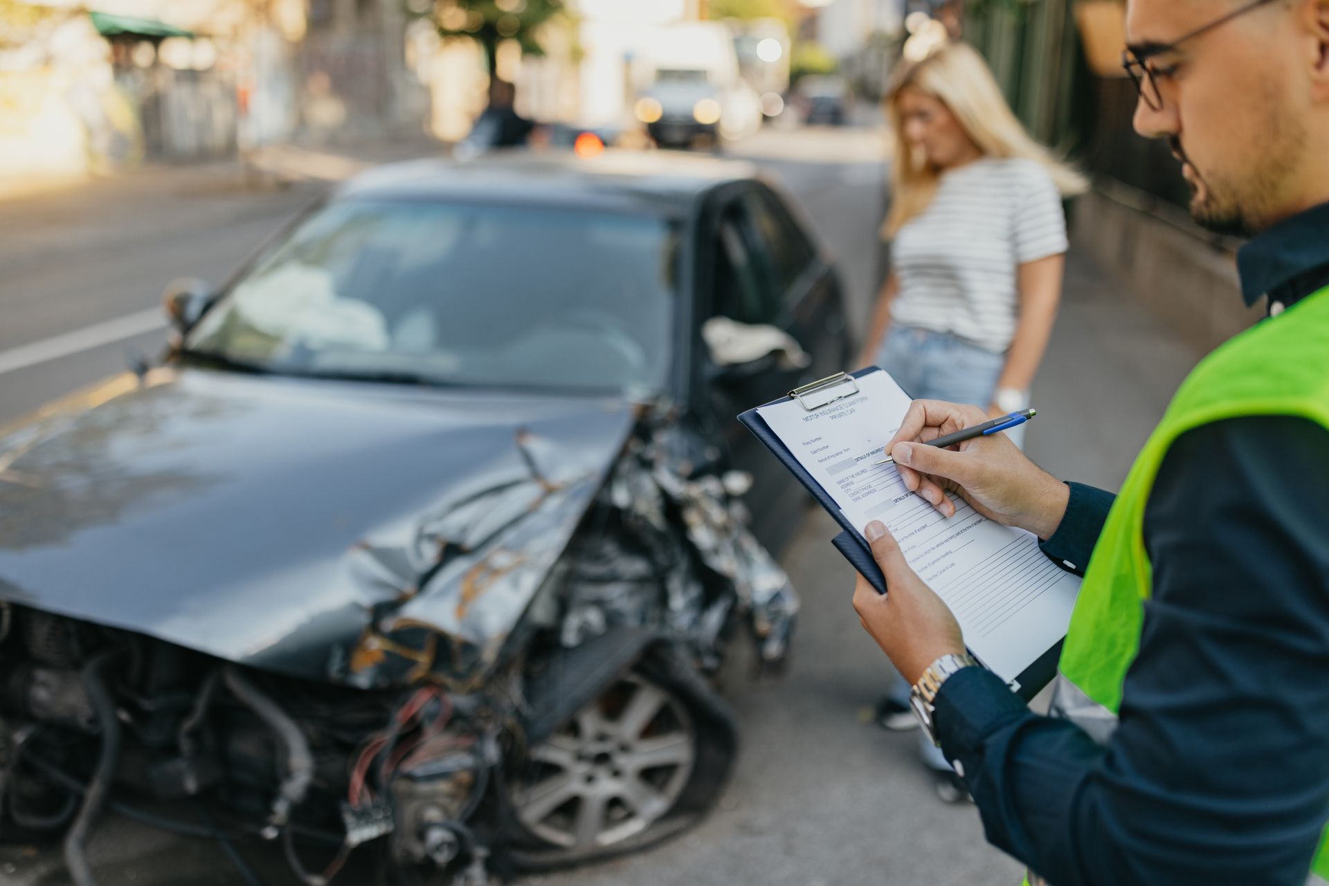 A man is writing on a clipboard in front of a damaged car.