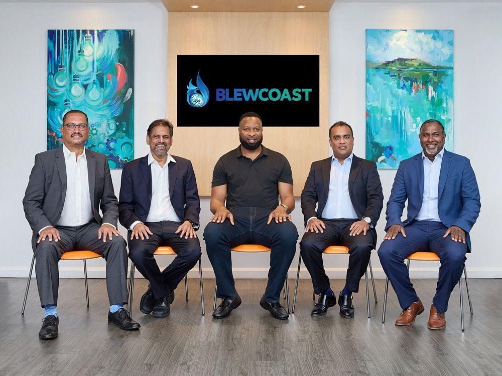 A group of men are sitting in chairs in front of a sign that says brewcoast.