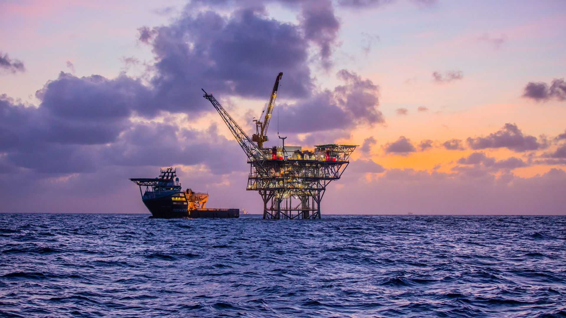 An oil rig in the middle of the ocean at sunset.