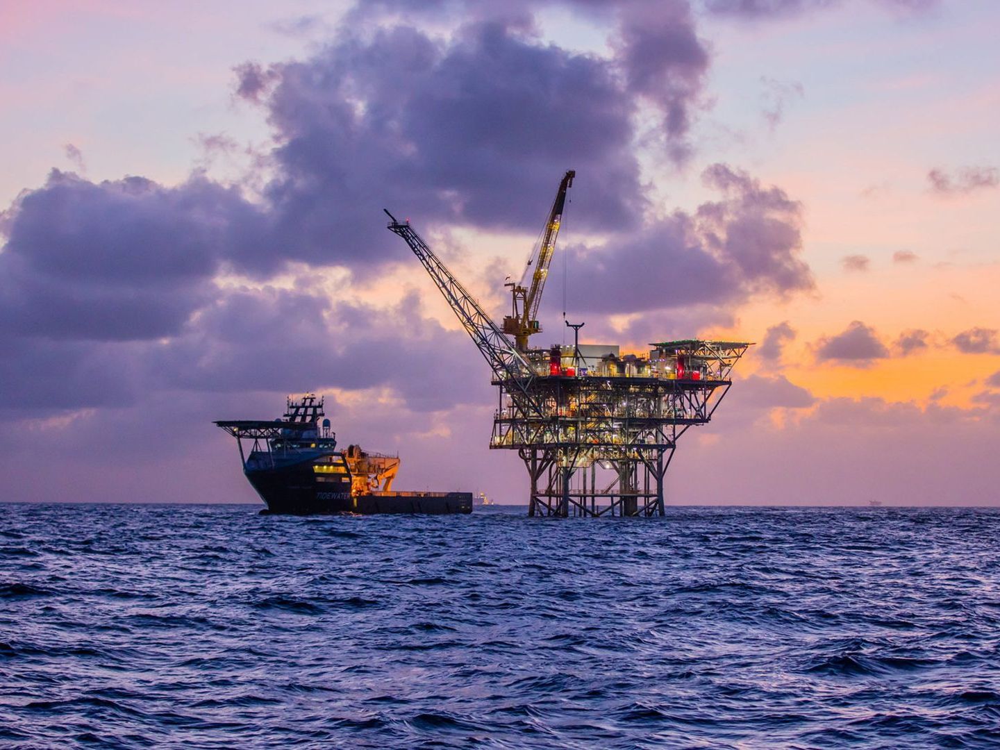 An oil rig in the middle of the ocean at sunset.