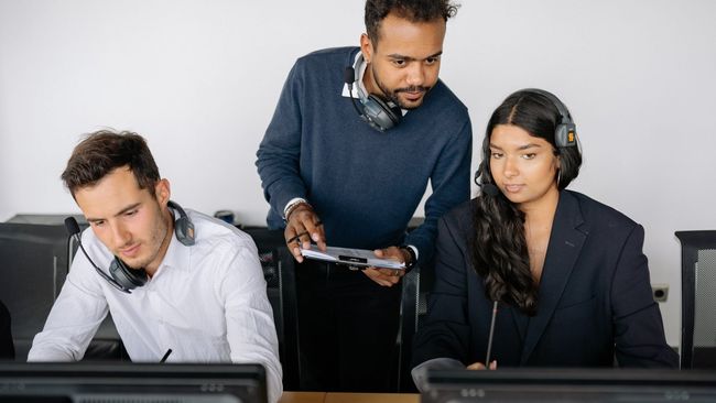 A group of people are sitting in front of computer monitors.