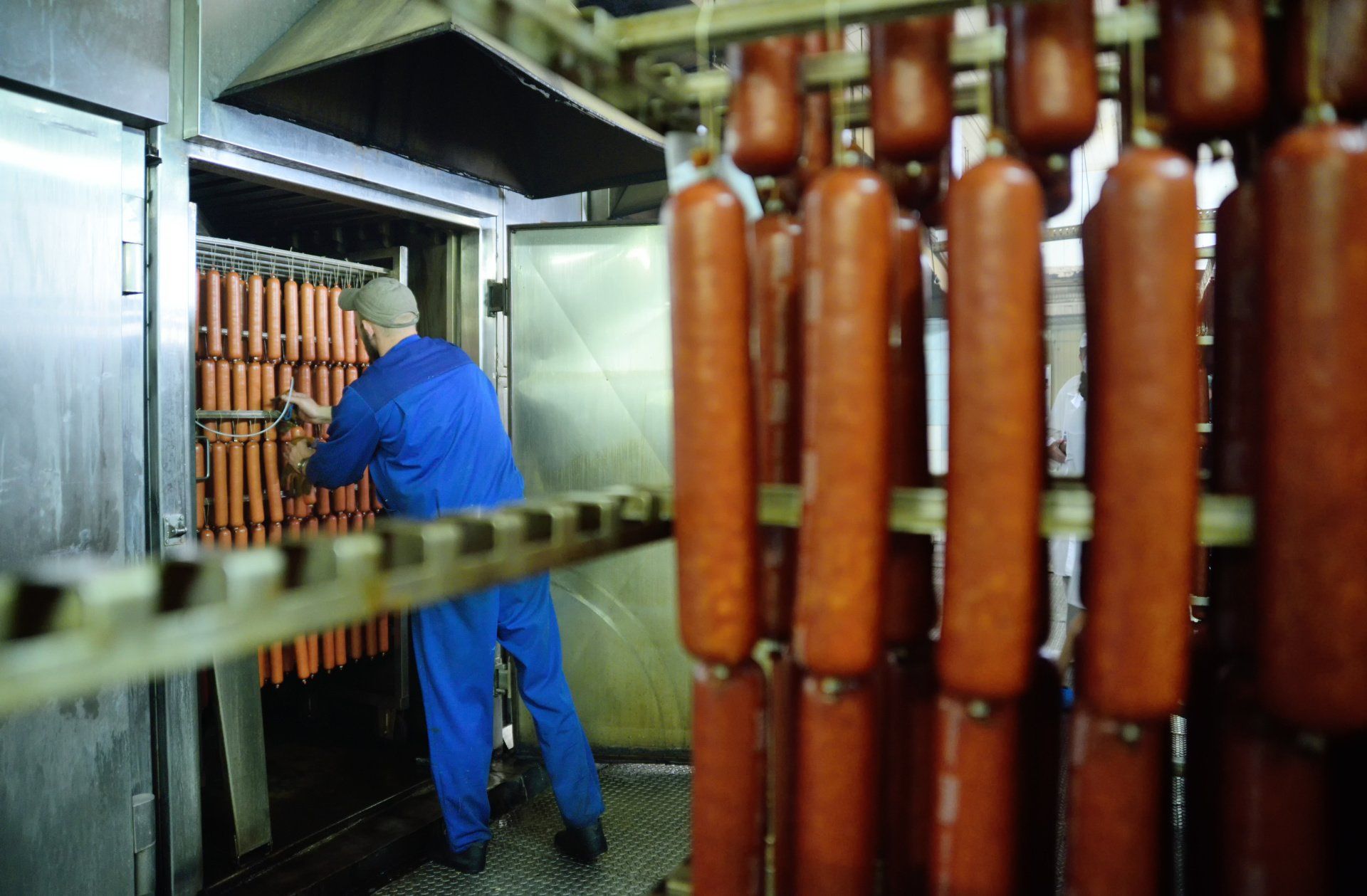 A man in a blue shirt is standing in a room filled with sausages.