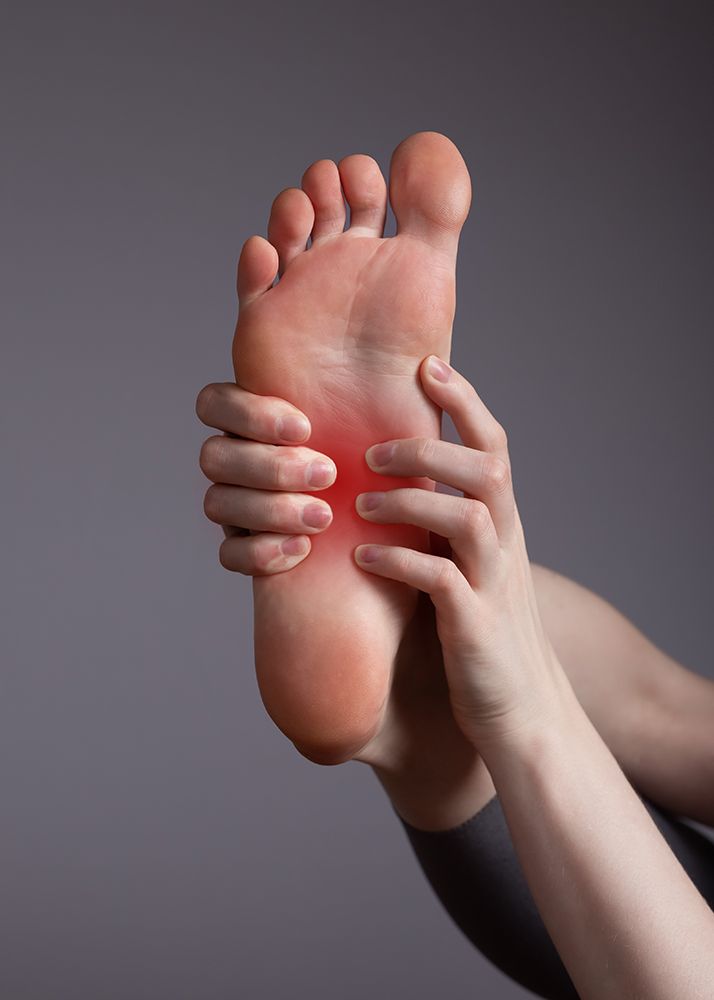 Person holding foot, red area indicating pain on the sole.