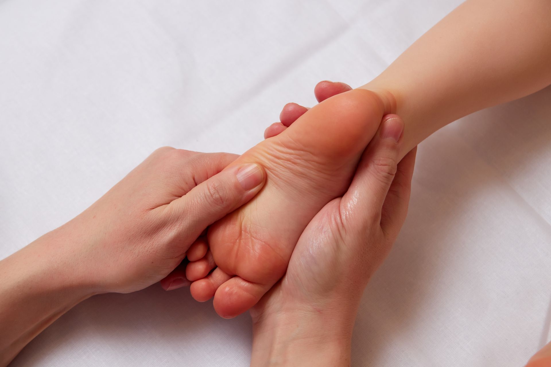 Hands massaging the sole of a foot on a white surface.