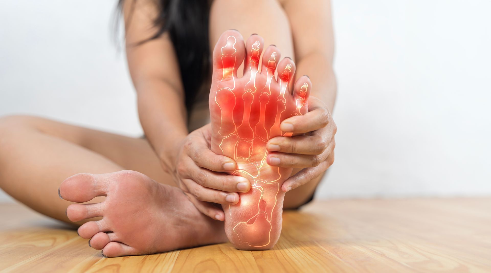 Woman holding foot with red highlighting, possibly indicating pain, sitting on wooden floor.