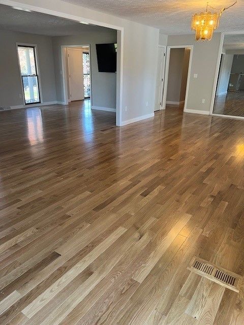 Hardwood floors in a spacious room with several doorways, featuring a TV and window, lit by natural and overhead light.