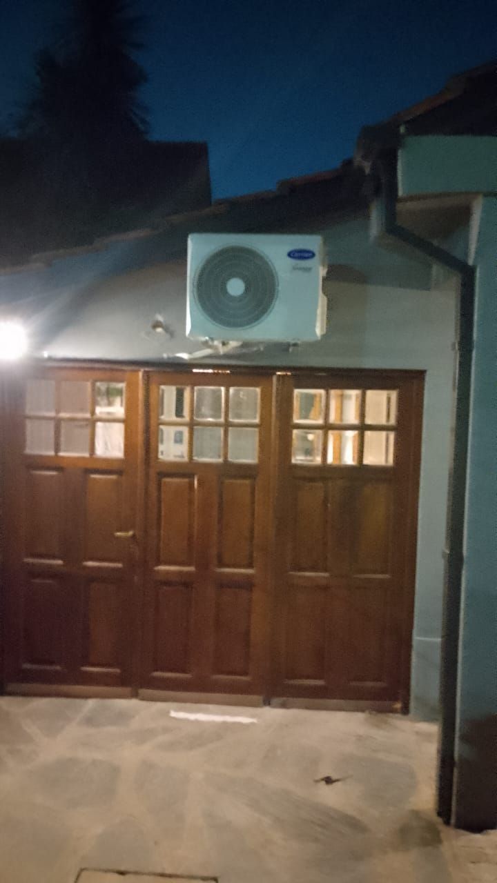 Puertas de garaje de madera, rematadas por un aire acondicionado Samsung, contra un cielo al atardecer.