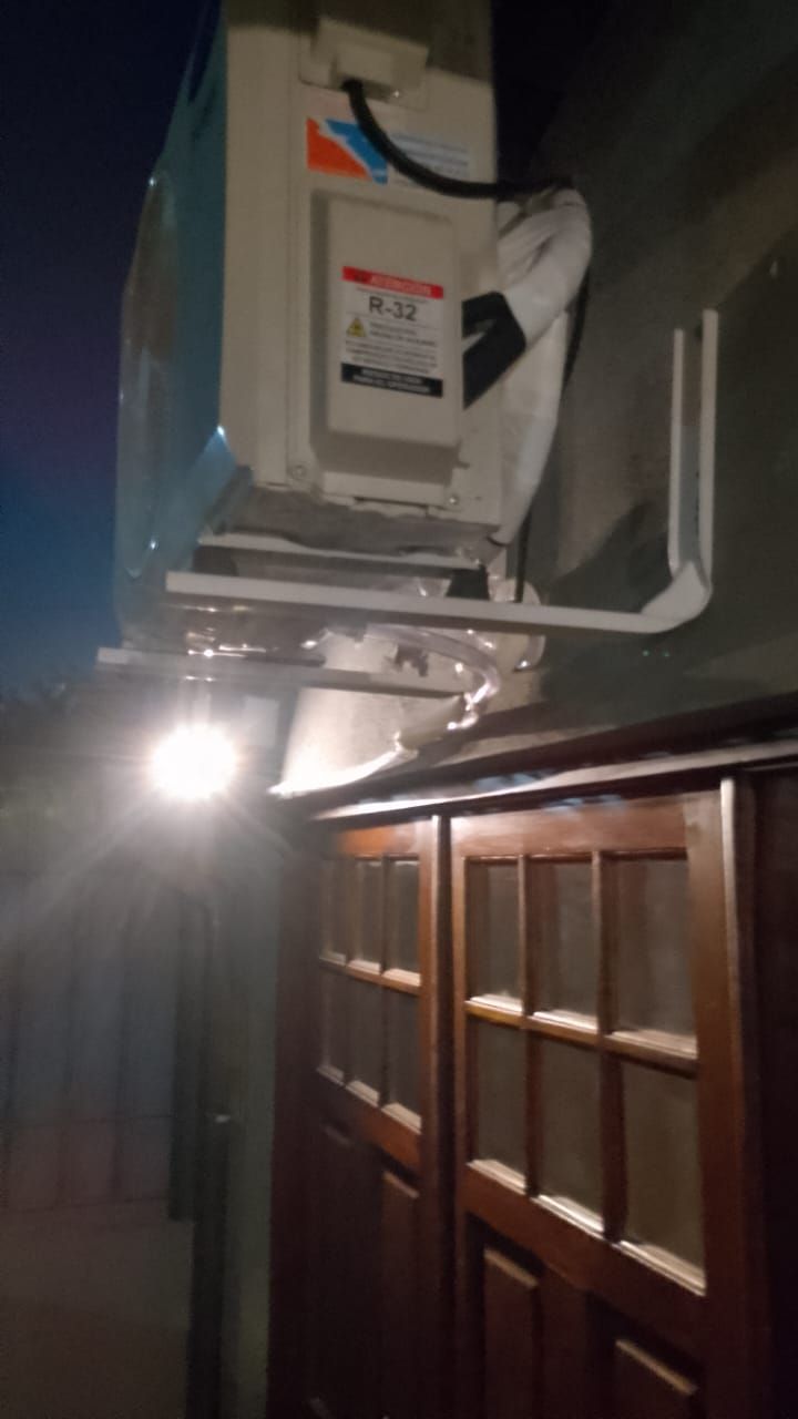 Una unidad de aire acondicionado está montada encima de un armario de madera oscura, iluminado por una bombilla.