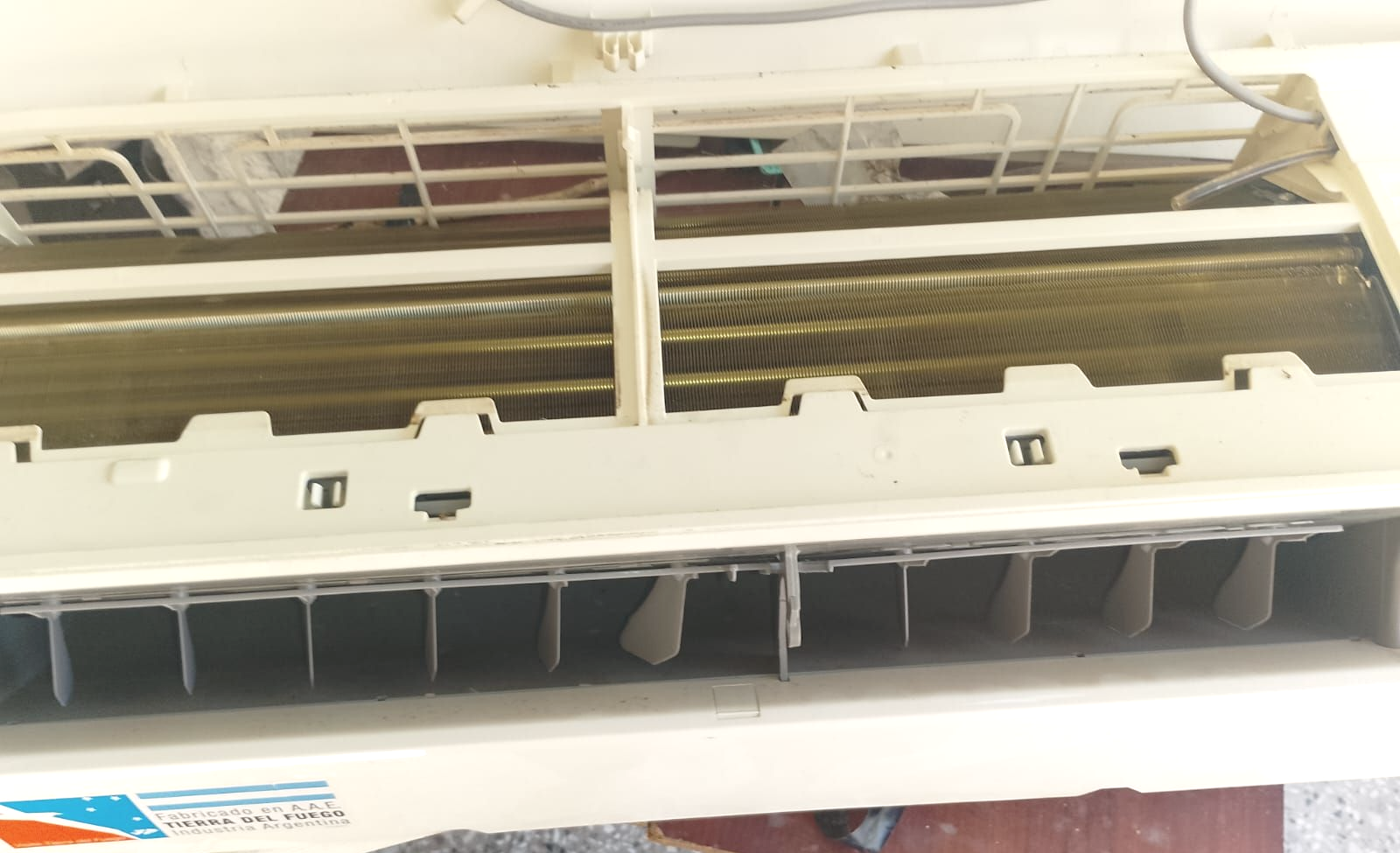 Primer plano del interior de un aire acondicionado. Carcasa de plástico blanco, aletas y serpentines de refrigeración visibles, y una serie de rejillas de ventilación.