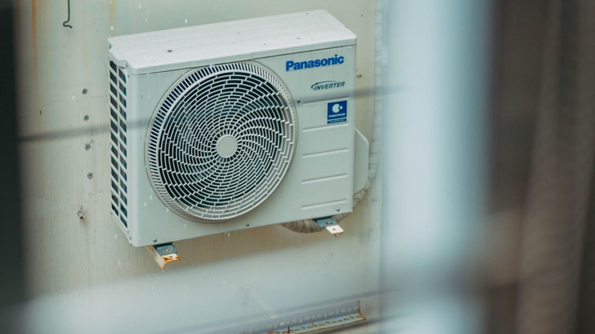 Unidad de aire acondicionado Panasonic montada en una pared desgastada, con un gran ventilador visible.