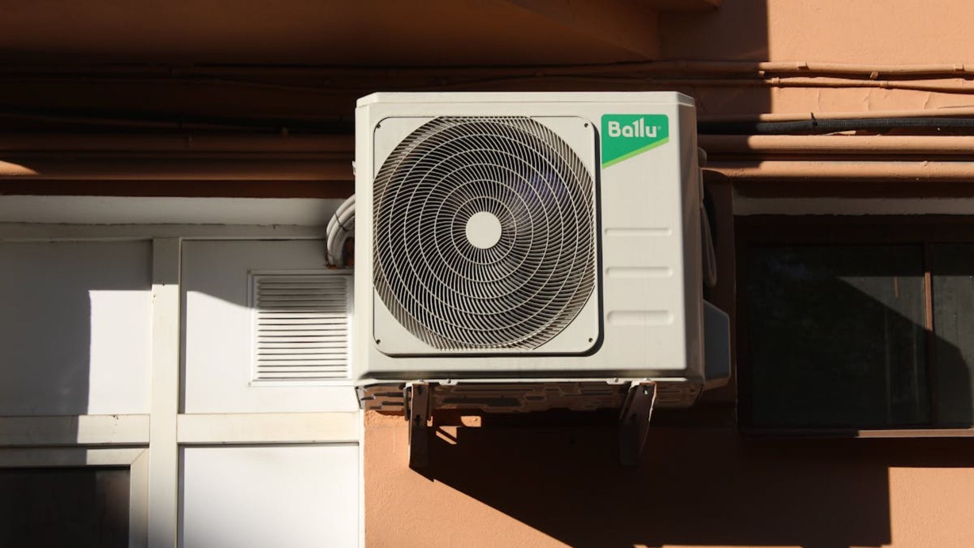 Aire acondicionado blanco montado en una pared exterior del edificio, con un ventilador visible.
