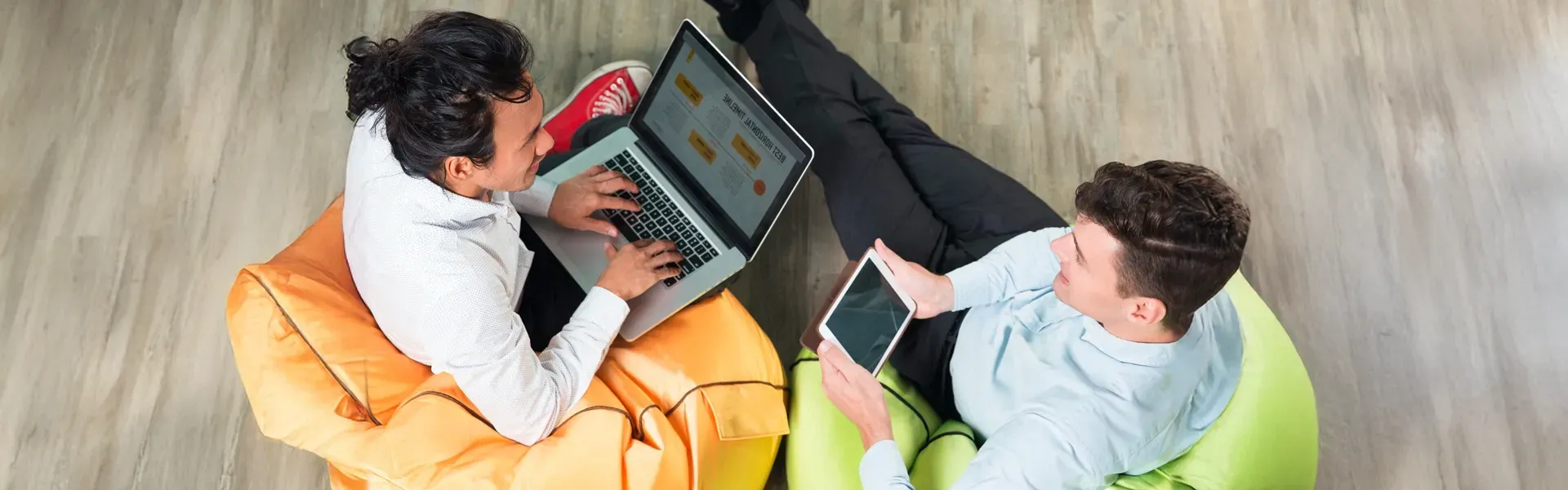 Two professionals sitting on bean bags collaborating on a digital project using a laptop and tablet 