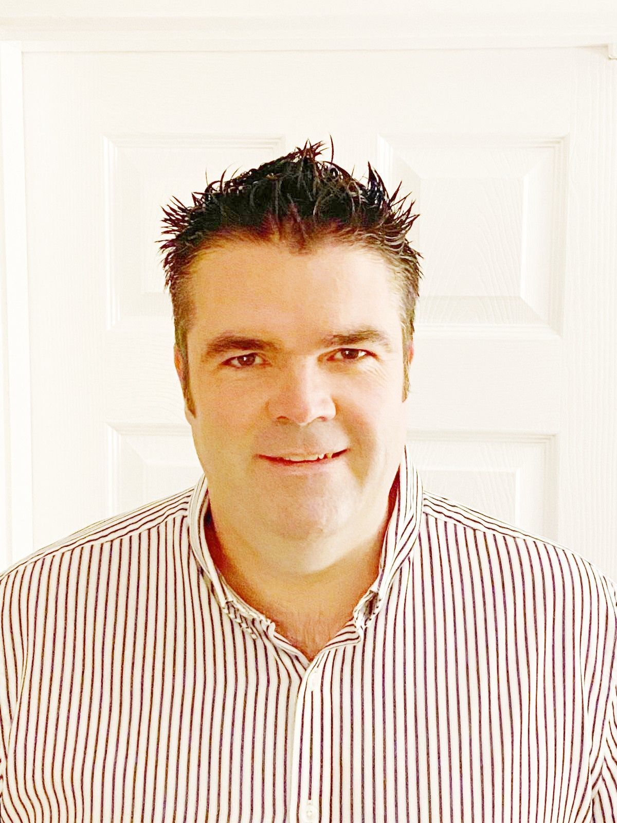 Matt  in a striped shirt is smiling in front of a white door.