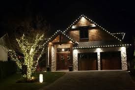 House at night decorated with white lights on roof and in a tree.
