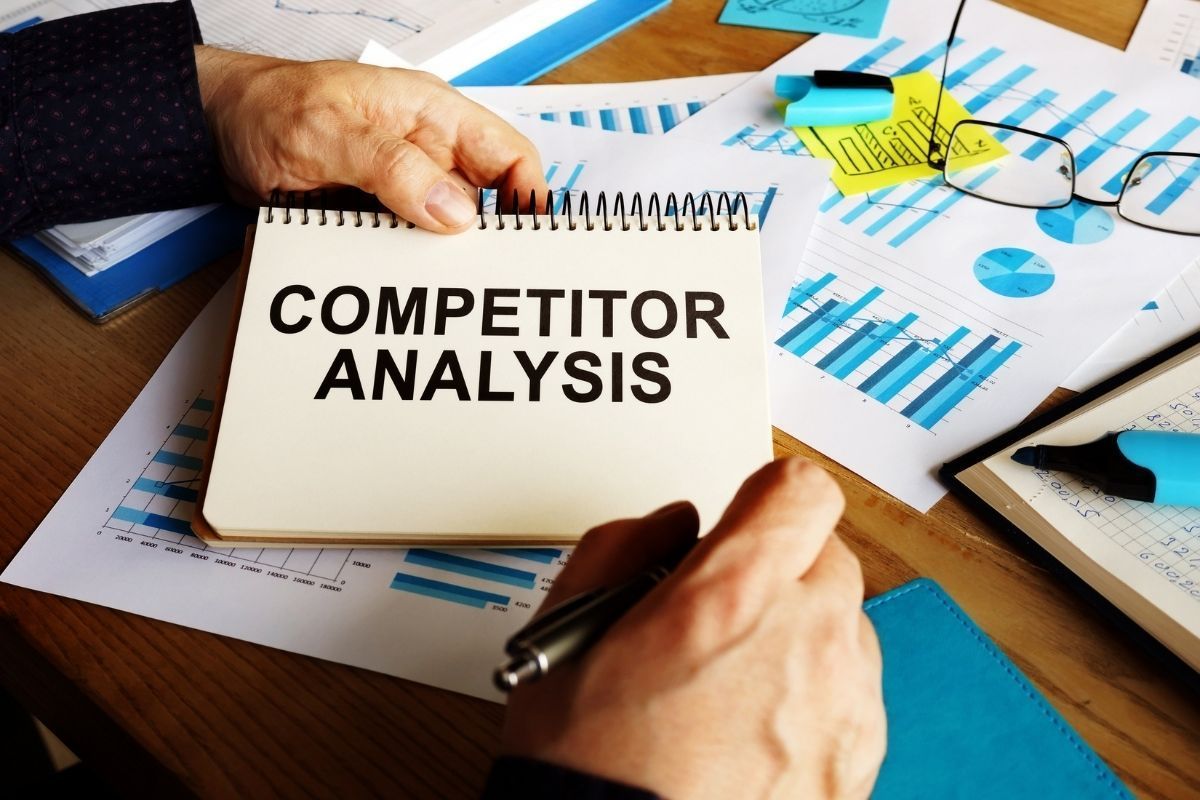 A person is writing in a notebook that says competitor analysis