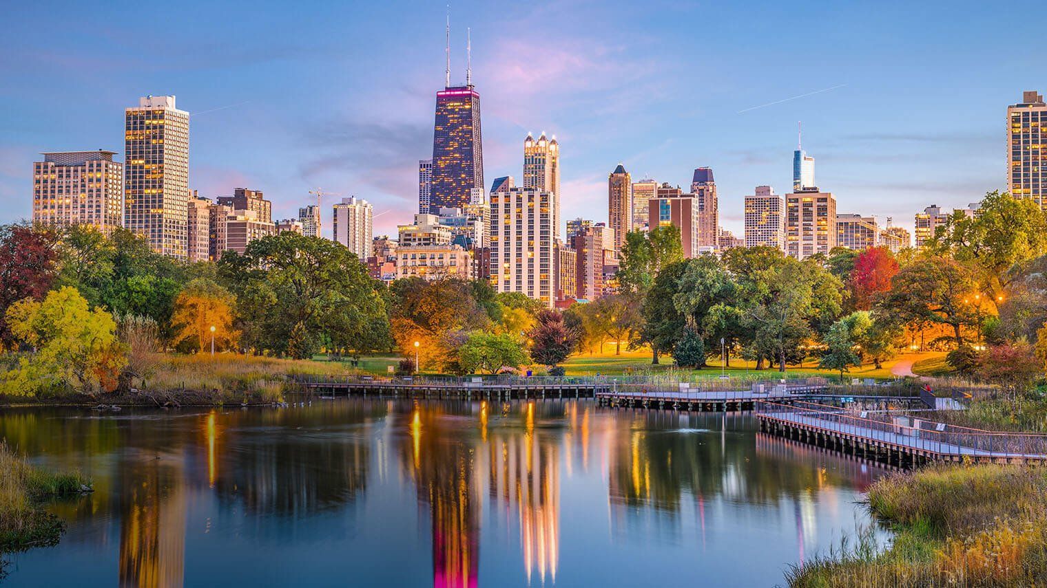 A city skyline with a lake in the foreground and a park in the background.