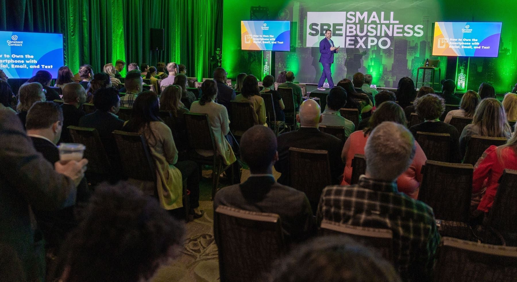 A large group of people are sitting in front of a stage at a small business expo.
