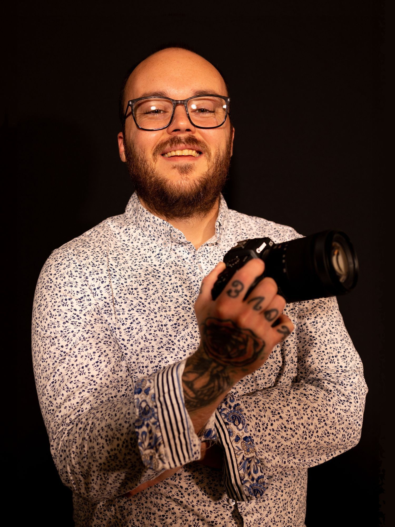 a man with a beard and glasses is holding a camera in his hand .